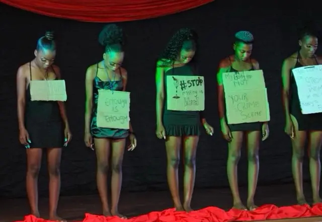 Young women on stage holding placards against gender-based violence